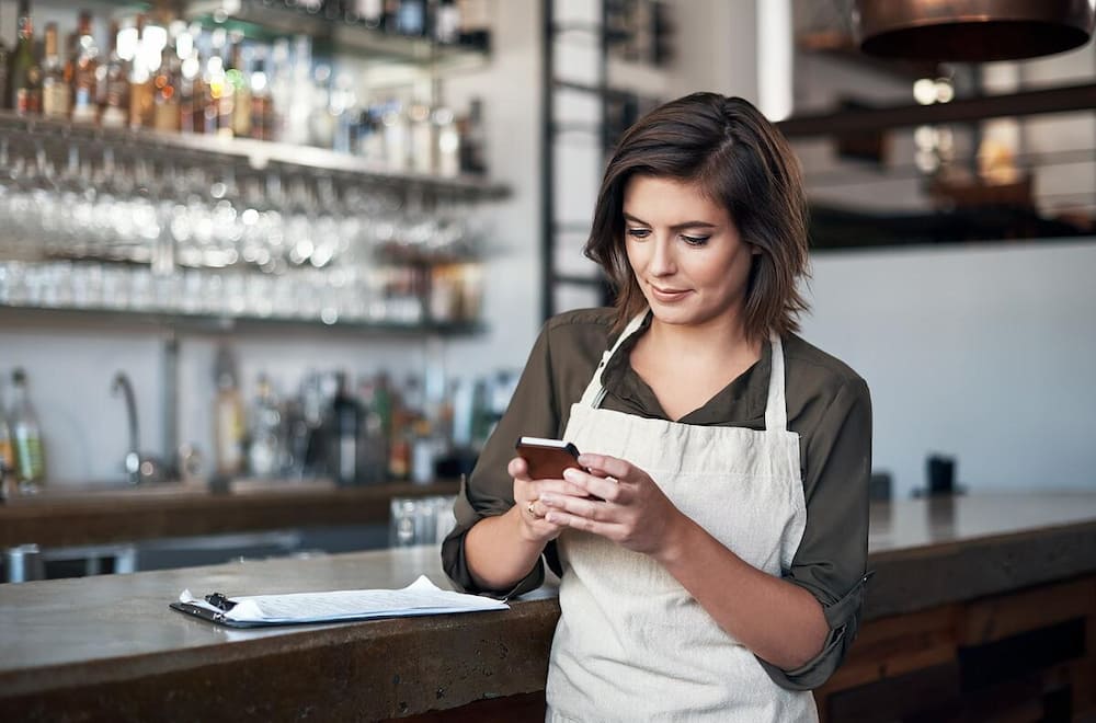 female small business owner in an apron looking at social media ads on her phone