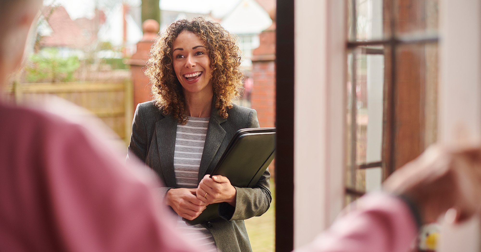 Woman with brown curly hair holding a laptop smiling
