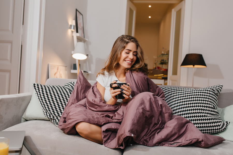 cheerful-woman-sitting-couch-with-blanket-cushions-smiling
