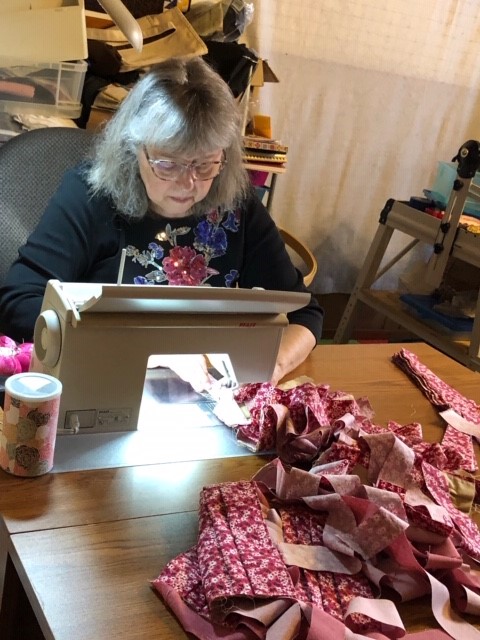 A person sewing at a table, surrounded by scraps of fabric.