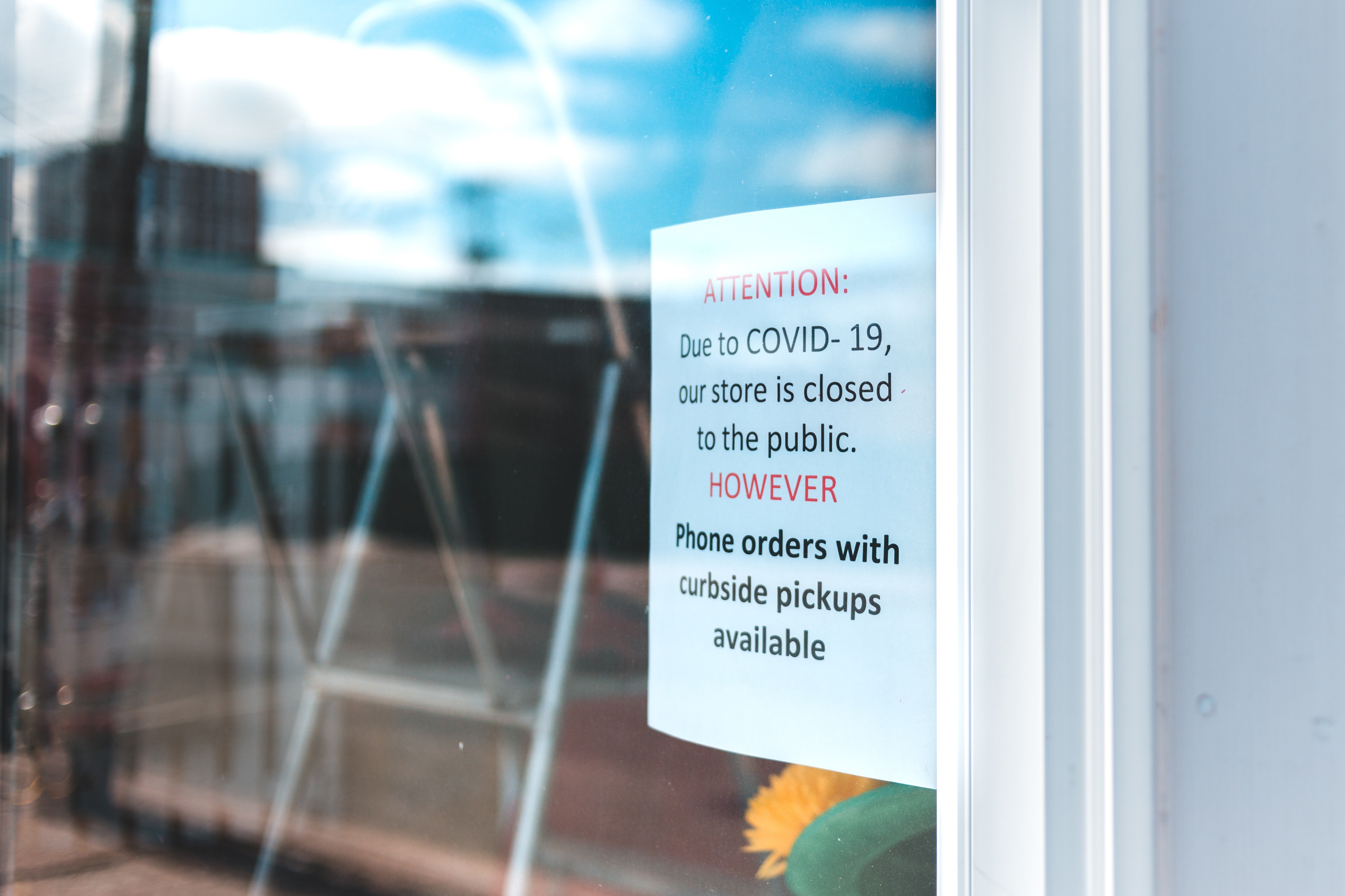 A white printed sign in a storefront window that says "Attention: Due to COVID-19 our store is closed to the public. However, phone orders with curbside pickups available"