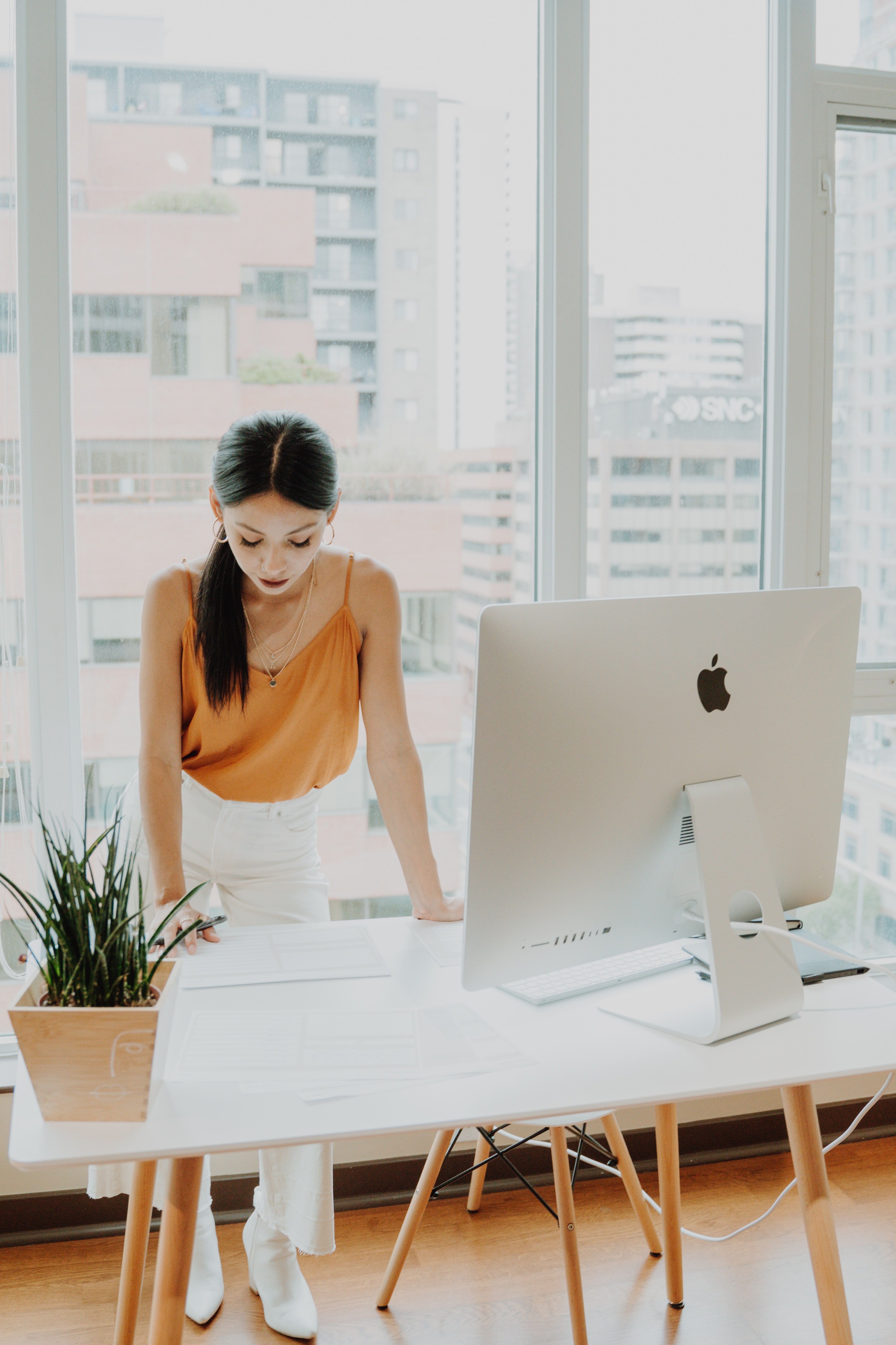 Image of a business woman standing behind a large desk looking over papers on the desk. She looks stressed and like she is making a big decision.