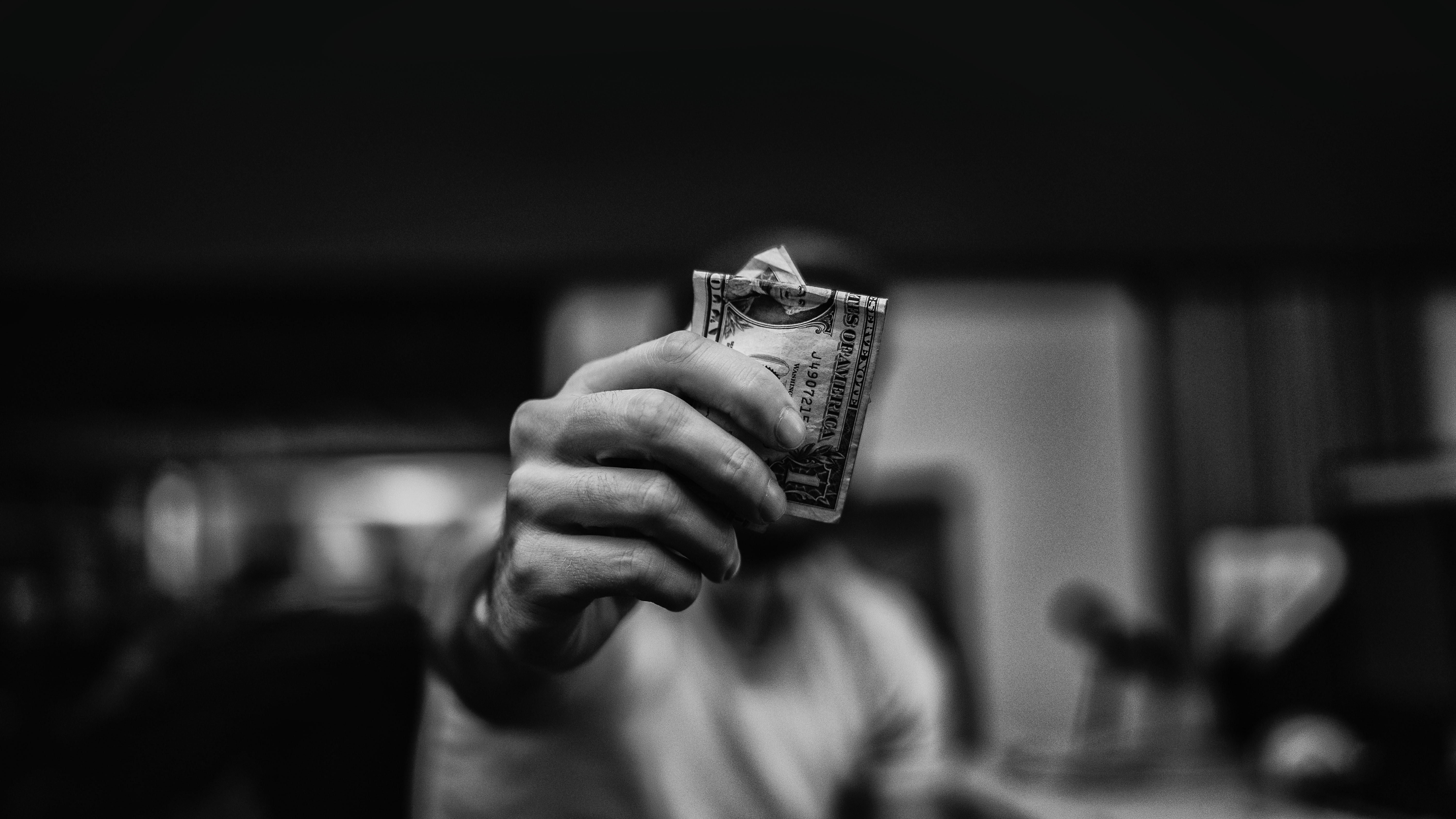 Decorative image in black & white of a masculine hand holding money up to the camera.