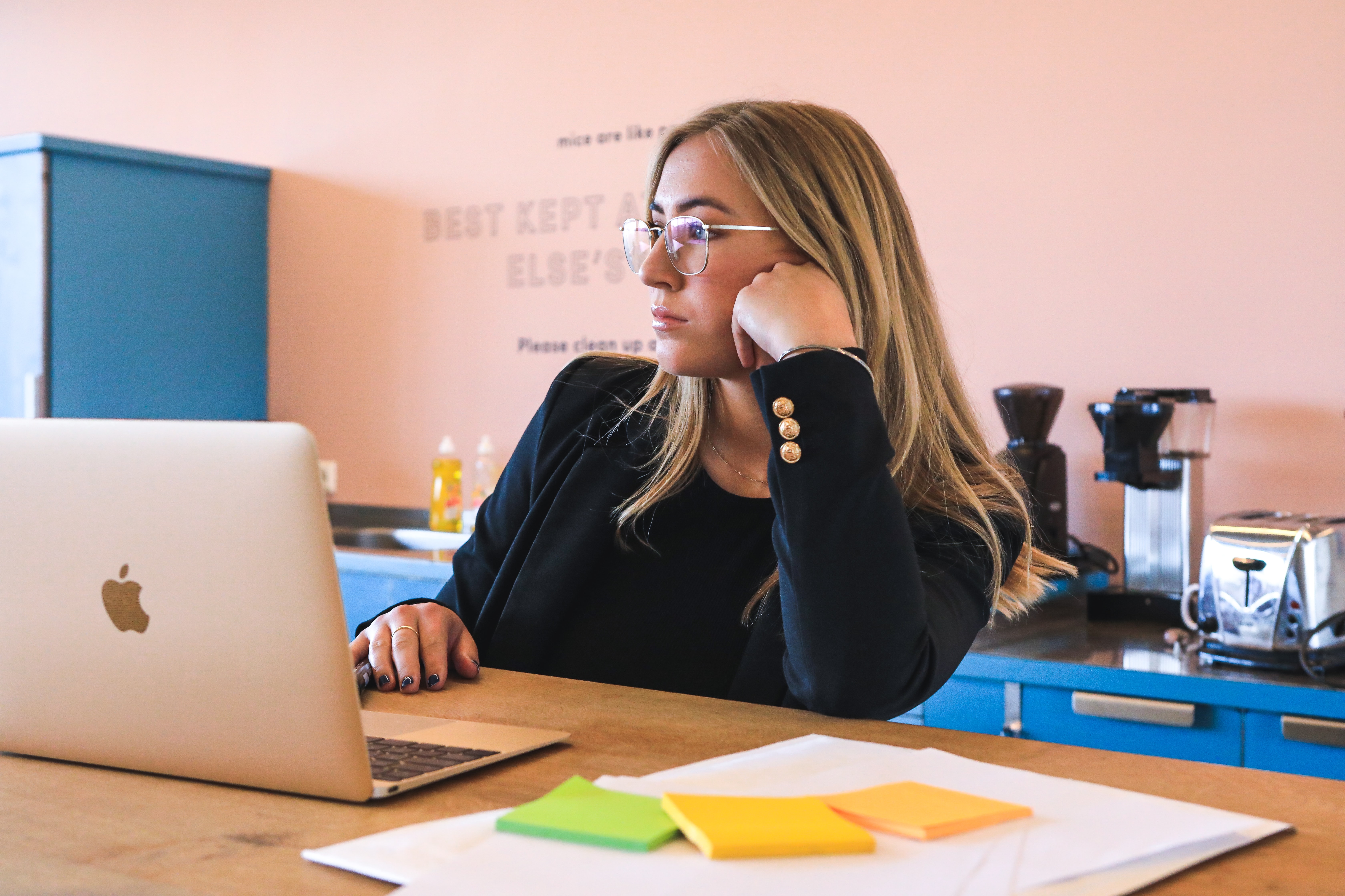 Woman sitting behind a macbook looking off into the distance, as if she is contemplating next steps.