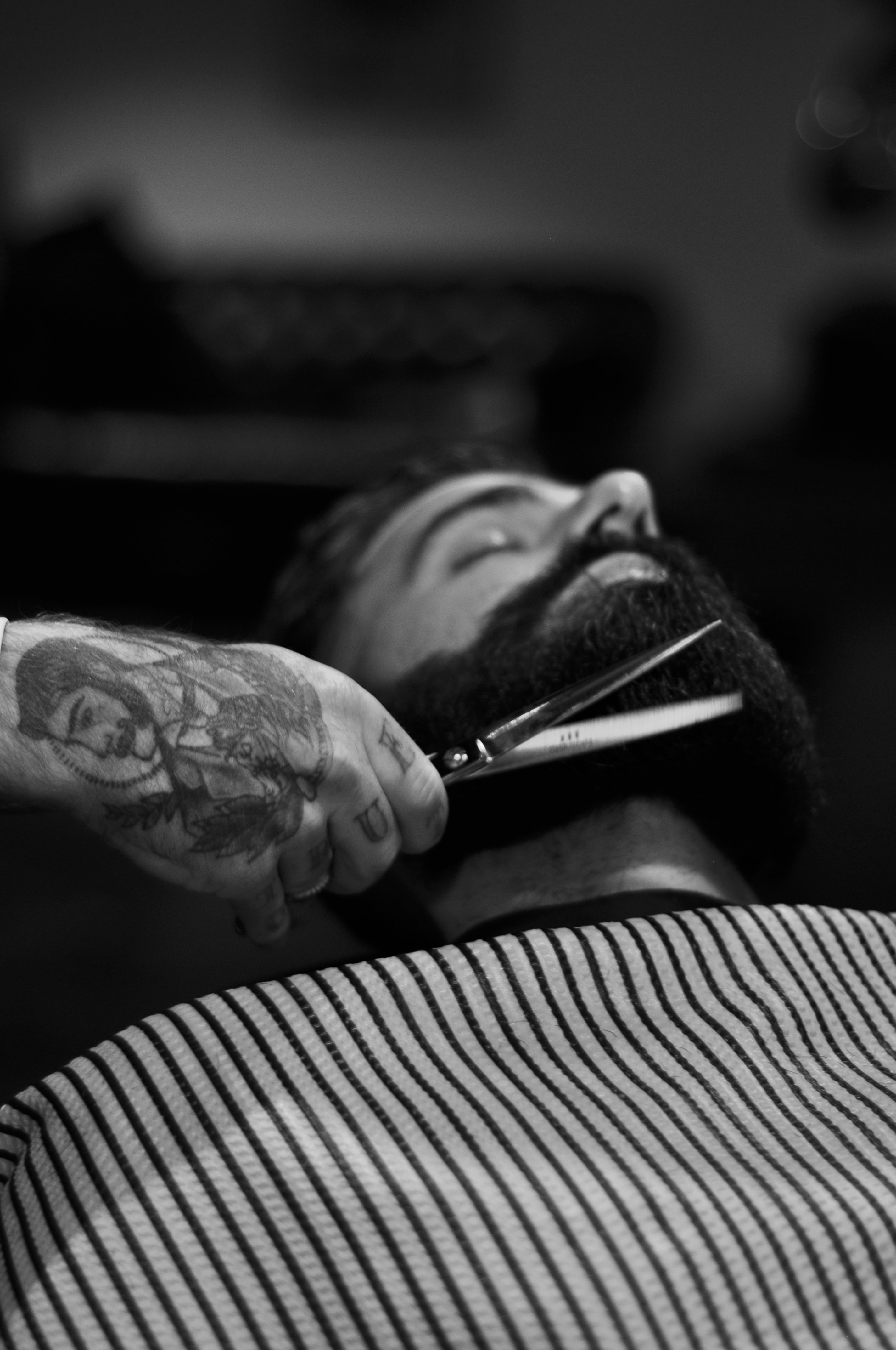 Image of a man with a beard lying back while another hand is holding scissors to trim the beard