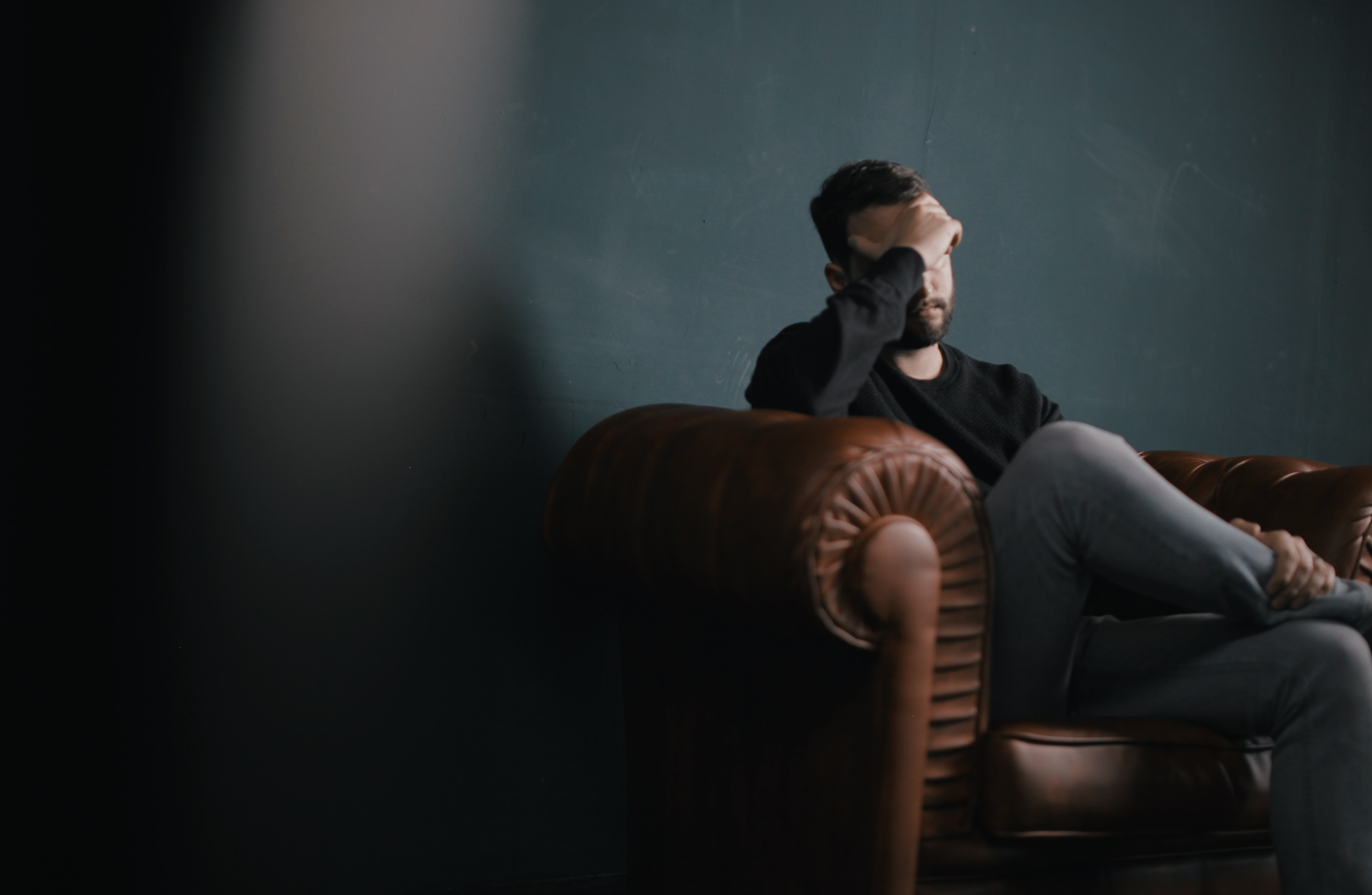 Image of a man sitting on a couch with his head in his hand. The sentiment is that he is stressed.