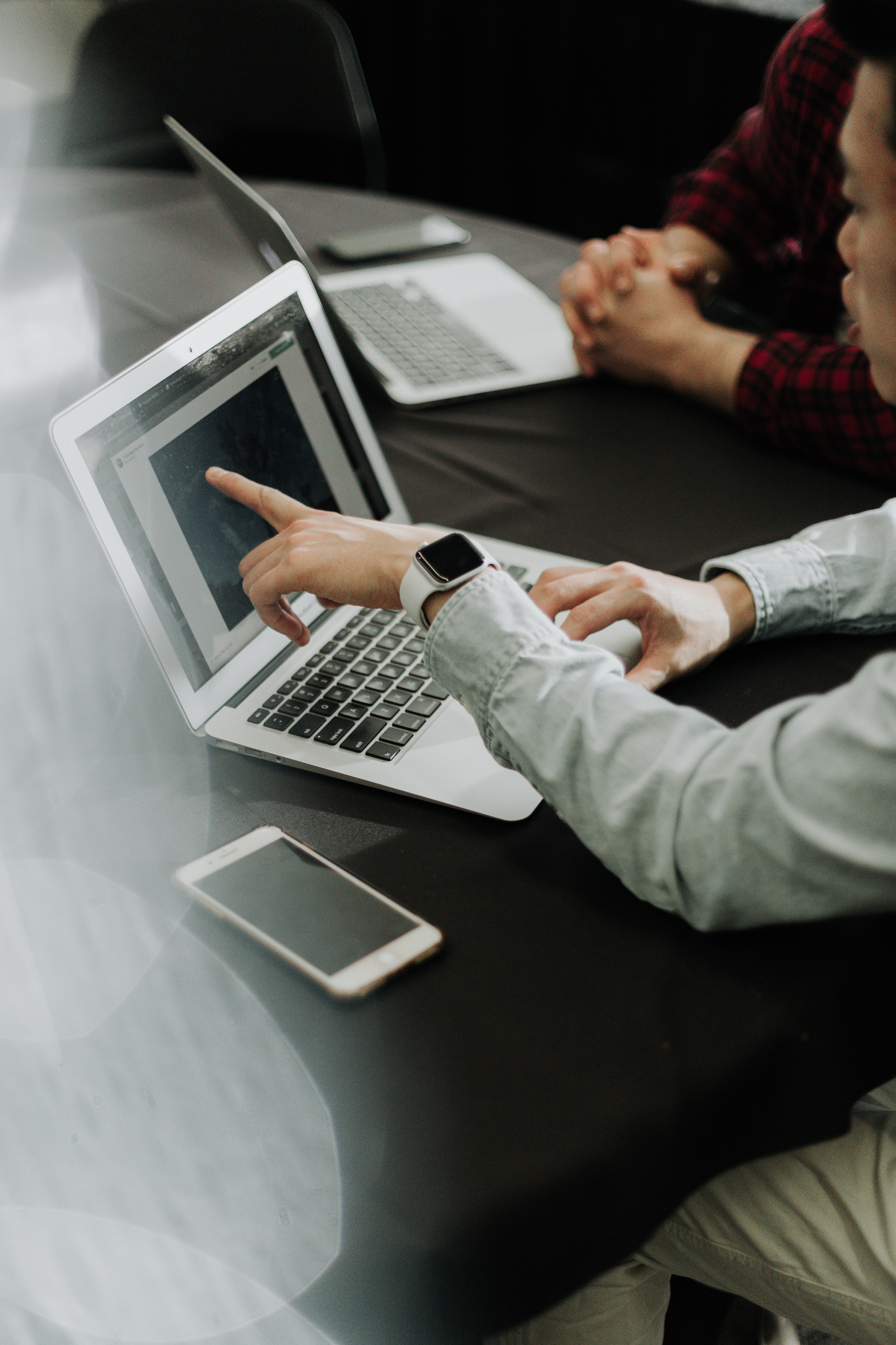 Two people sitting in front of laptops. One is pointing to something on the screen and explaining to the other person.