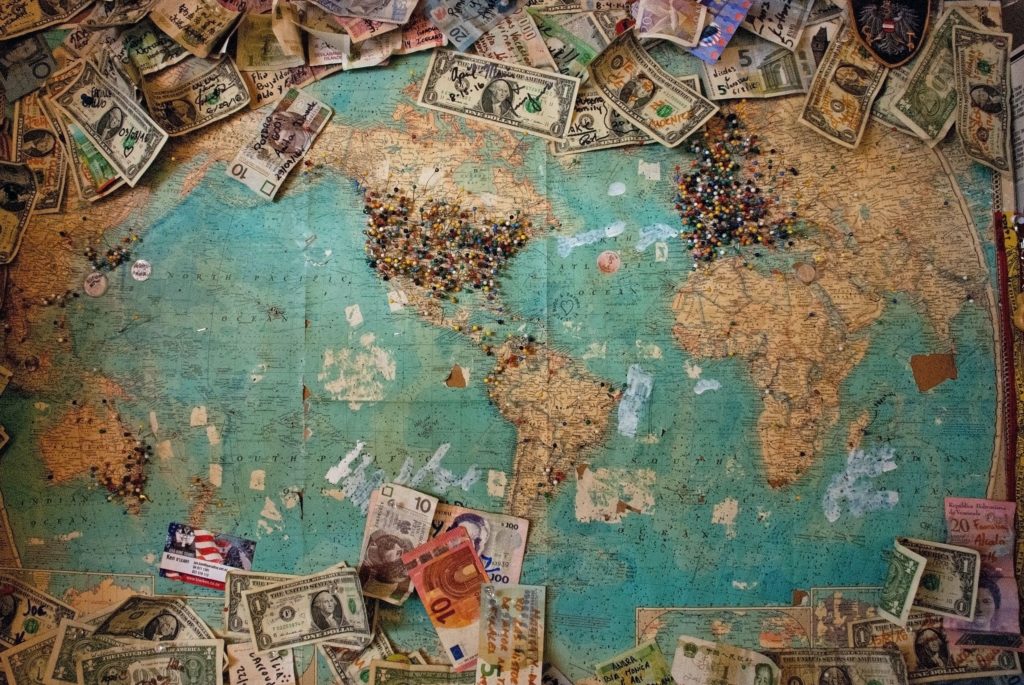 Weltkarte mit bunten Pins und Geldscheinen rundherum