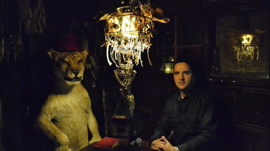 Evan Panagopoulos an einem Tisch mit einer ausgestopften Löwin
