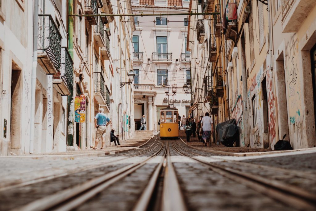 Inmitten der engen Straßen Lissabons in Portugal fährt eine kleine gelbe Straßenbahn.