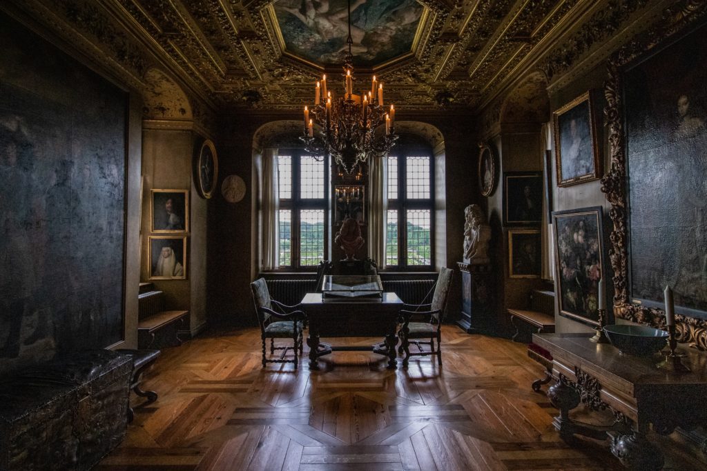 a very regal looking place, a living room with paintings on the wall, a table and stairs in the middle of the room 