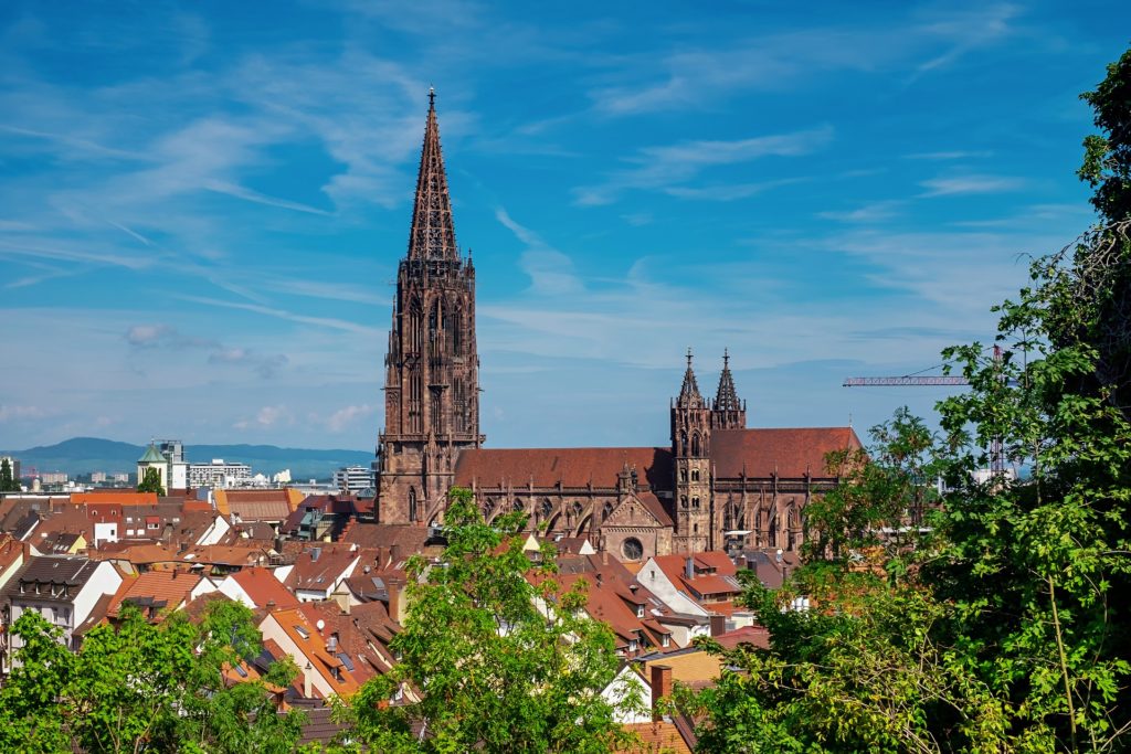 a shot of the city Freiburg with beautiful blue skies and a cathedral with green trees around it in one of the largest federal states in Germany