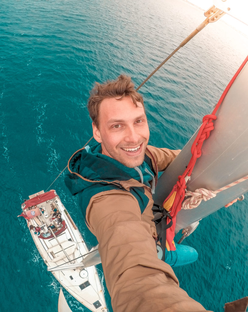Mitglied der Crew macht Selfie auf dem Mast, unter ihm Boot und Wasser