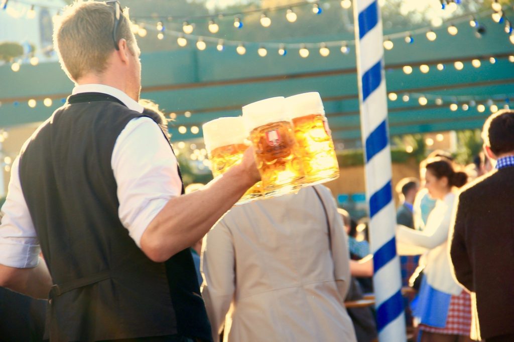 Man in traditional german clothing holding three beer mugs during Oktoberfest.