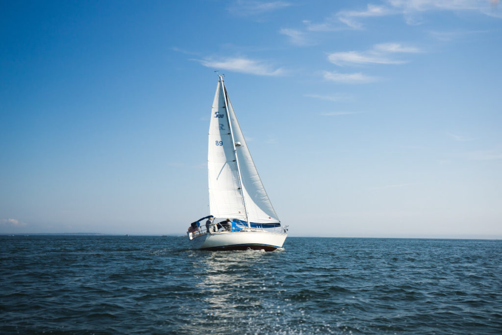Weißes Segelboot auf offenem Gewässer vor fast wolkenlosem Himmel 