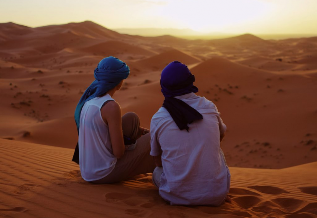 2 travel partners sitting together in the desert, happy to have found each other.