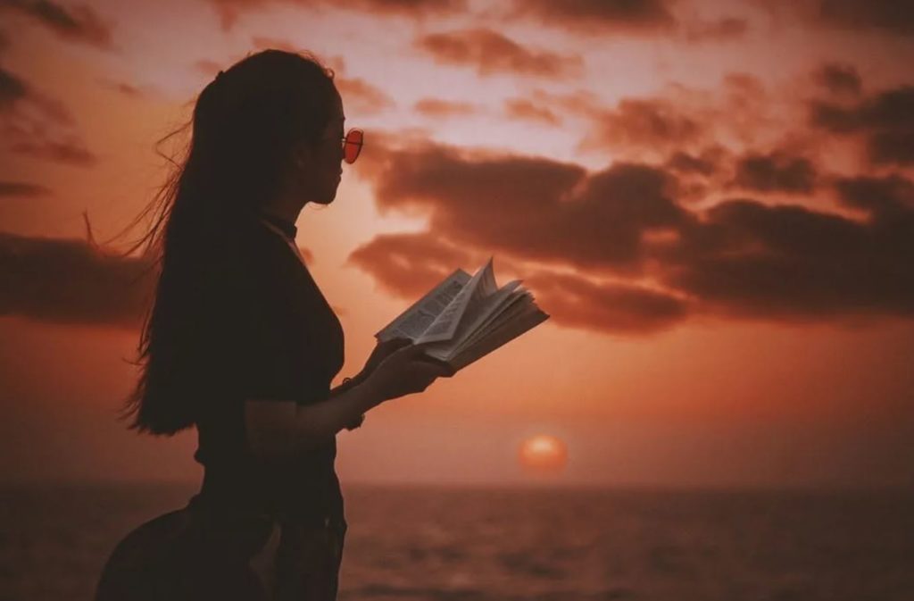 Frau liest ein Buch am Meer bei Sonnenuntergang