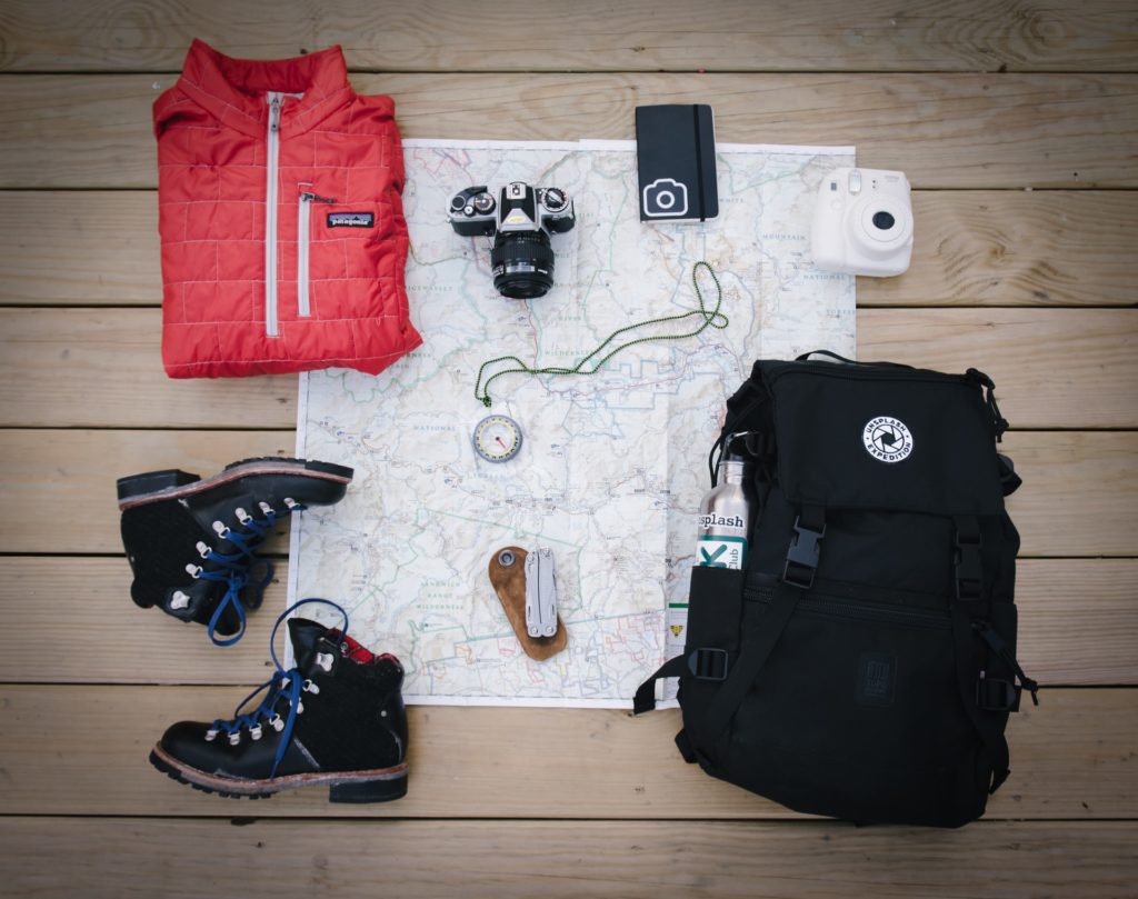 Schwarzer Rucksack, Jacke, Schuhe und Kleinigkeiten ausgebreitet auf Landkarte