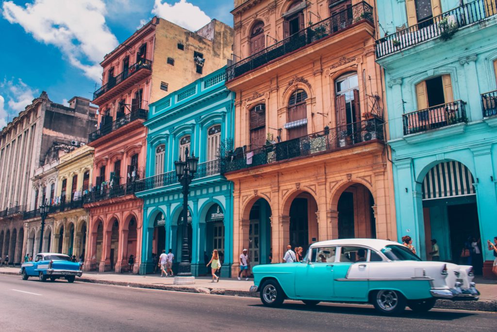 Bunte Häuser in Havanna mit zwei blauen Autos und Menschen
