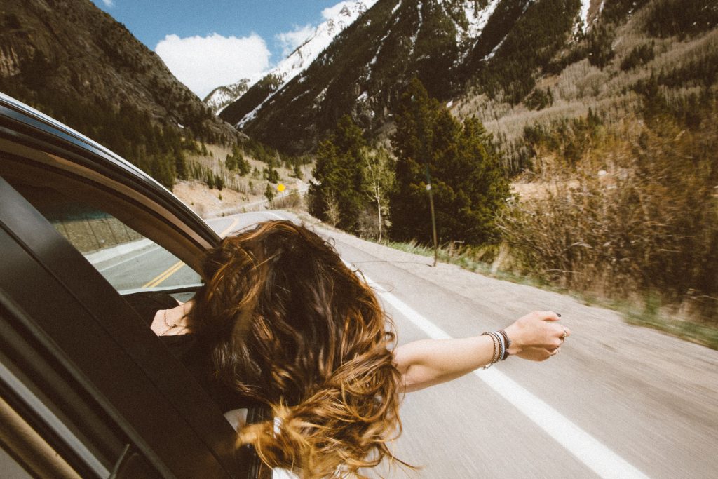 Girl with head out of car window in mountainous background