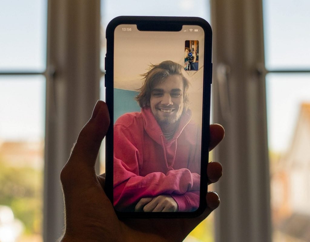 A man holding his cell phone and making a video call with a friend.