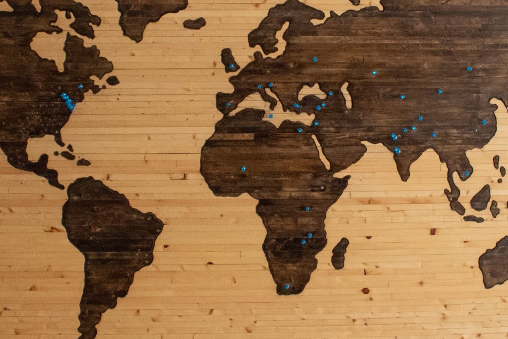 Weltkarte aus Holz in braun mit blauen Pins.
