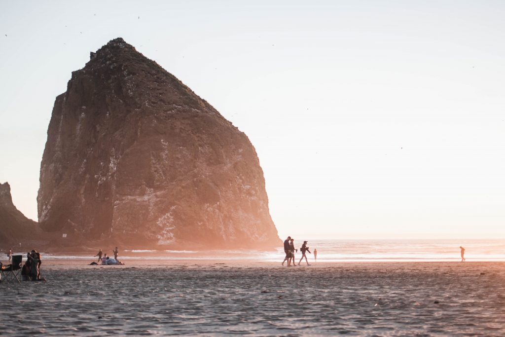 Haystack Rock in Oregon with people walking at sunrise