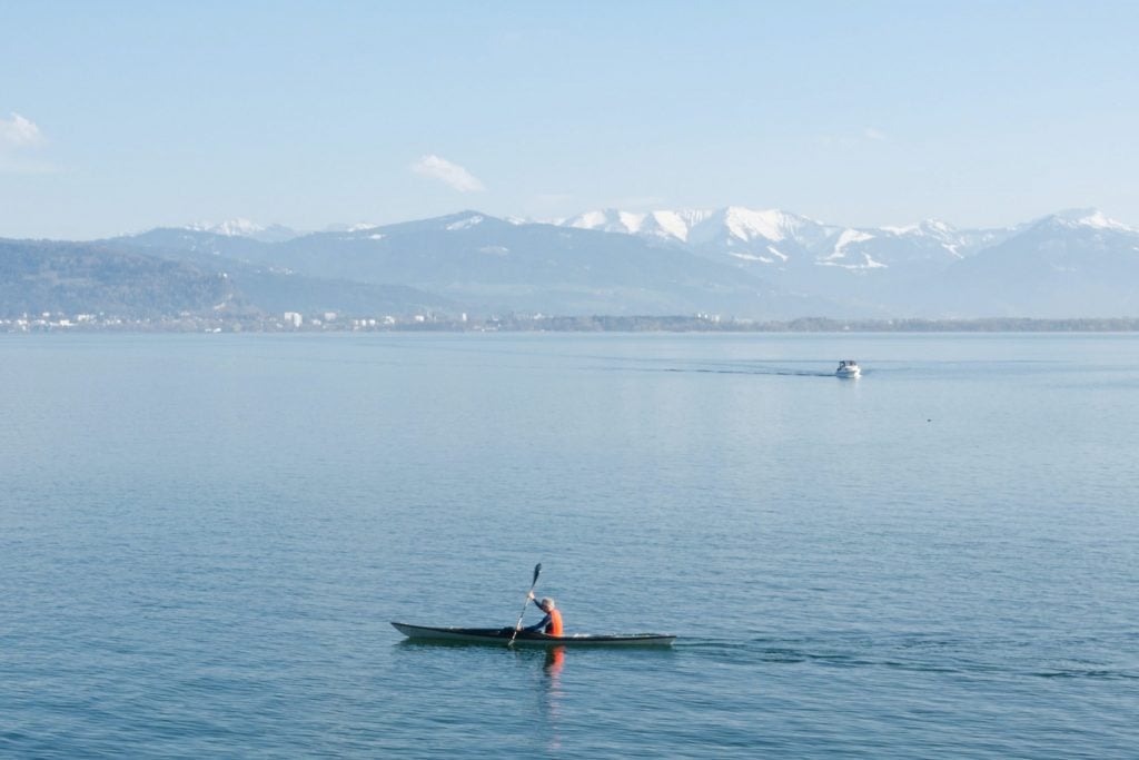 Blick auf den Bodensee und auf die Alpen mit einem Kanufahrer.