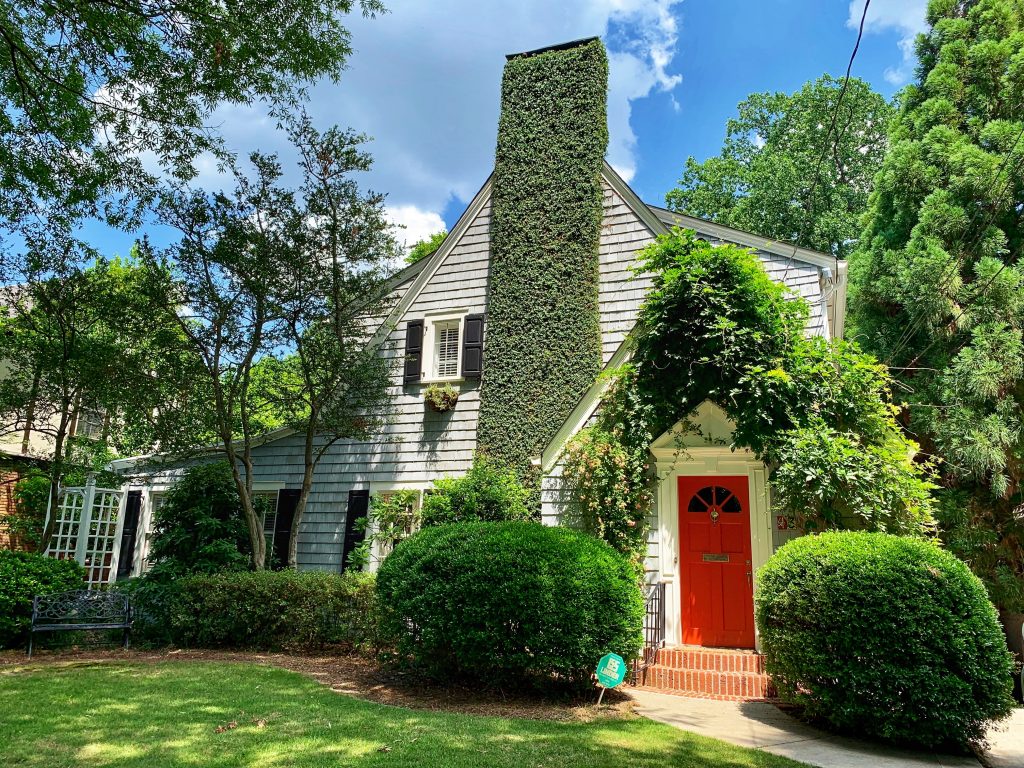 A house covered in green plants with a red door in the day time.