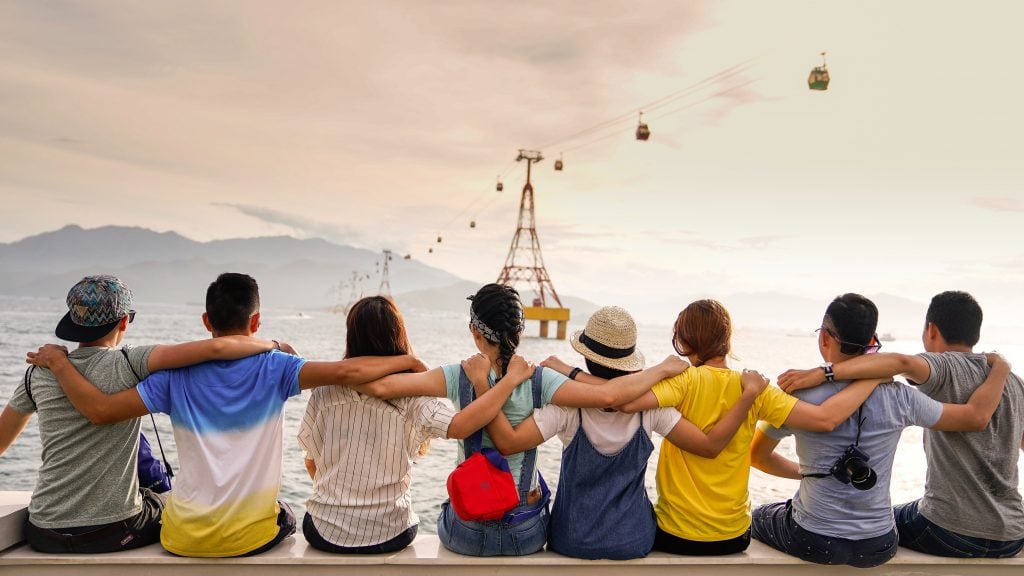8 junge Leute sitzen auf einer Bank, halten sich in den Armen und genießen die Aussicht auf ihrer Gruppenreise.