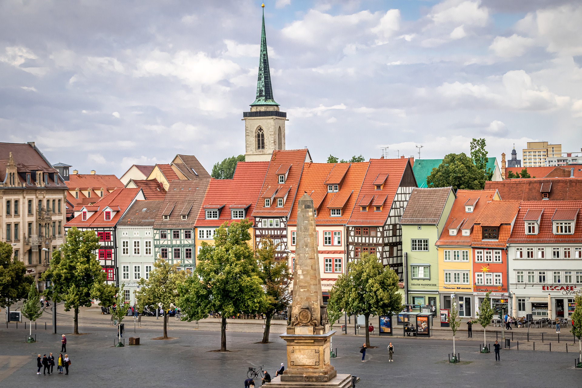 Der Domplatz in Erfurt mit roten Zinnen und Fachwerkhäusern. Im Hintergrund sieht man eine Kirche. 
