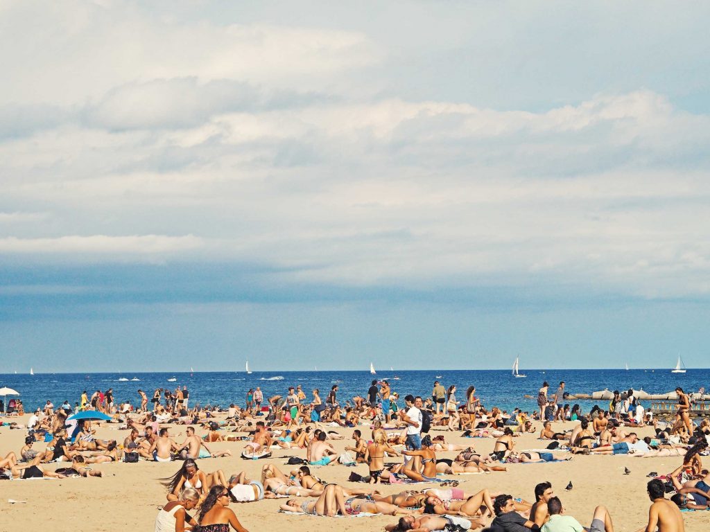Plan your 2021 travel to Spain with other travelers laying on the beach on a hot summer day.