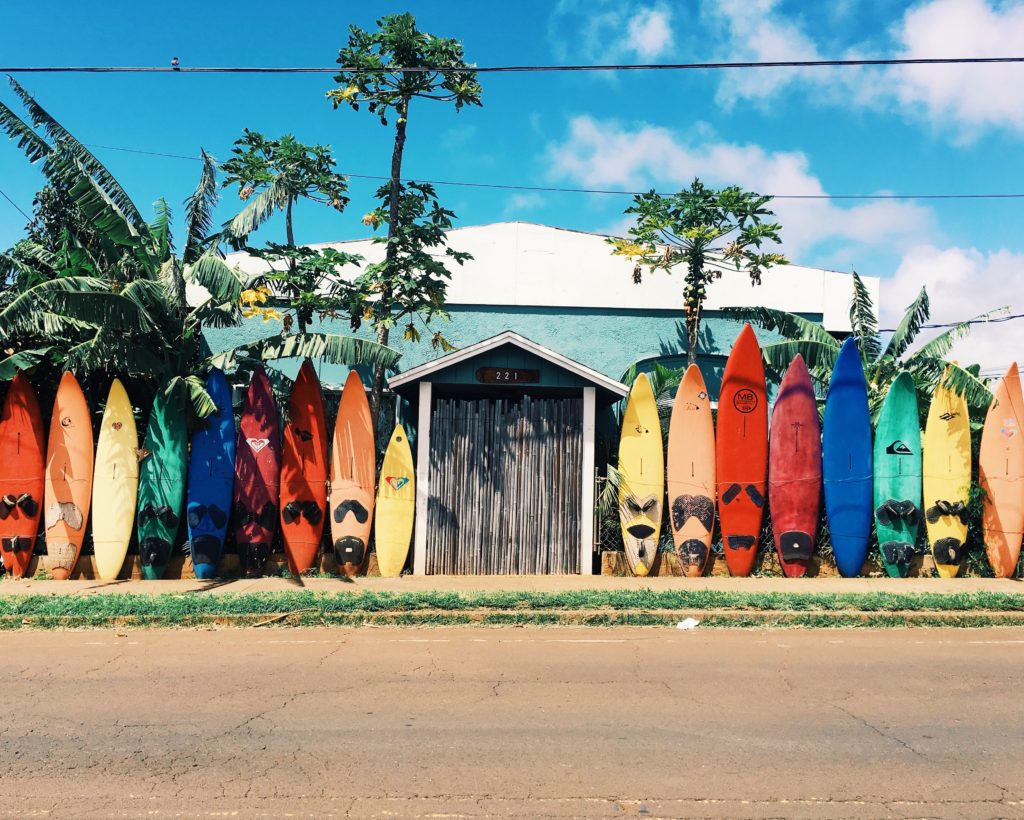 viele bunte surf boards die an ein Haus angelehnt sind mit blauem Himmel 