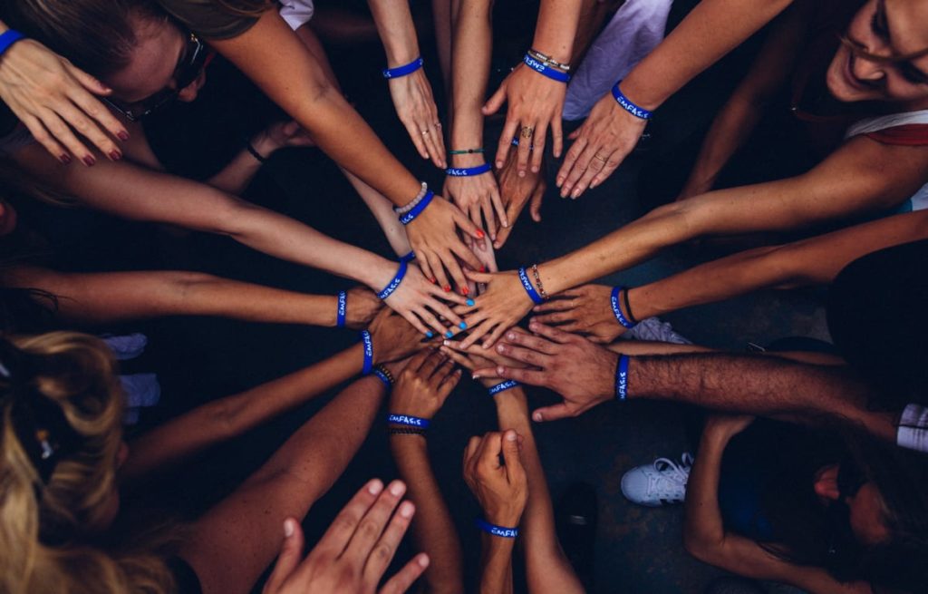 Viele Hände liegen aufeinander und an jedem Handgelenk ist ein blaues  Armband zum Zeichen der Zugehörigkeit 
