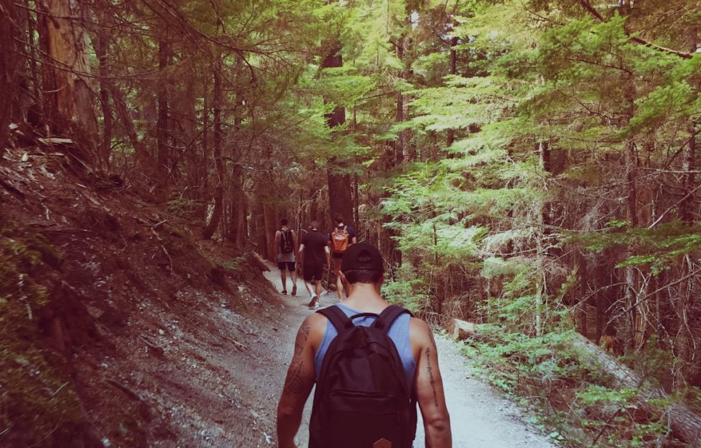 a man walking behind 3 other men on a hiking trail in the forest