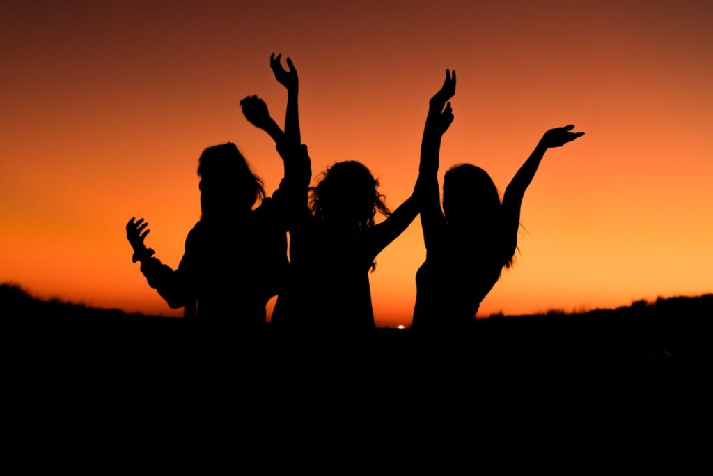 Drei Frauen in einer Gruppenreise tanzen im späten Sonnenuntergang