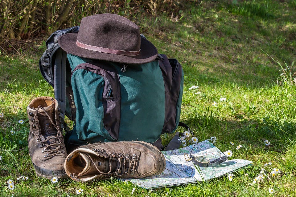one bag travel with a blue backpack and a brown pair of boots and hat on the grass