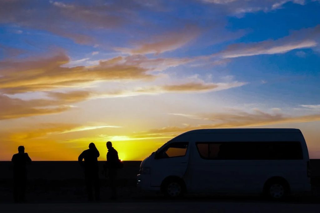 three people standing outside a van during the sunset