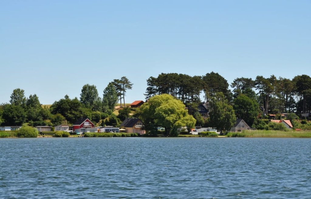Dorf auf einem grünen Ufer and einem blauen See unter strahlend blauem Himmel. 