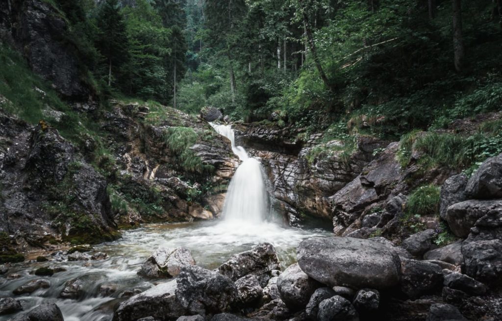 Fluss in Bayern mit kleinem Wasserfall inmitten eines dunkelgrünen Waldes