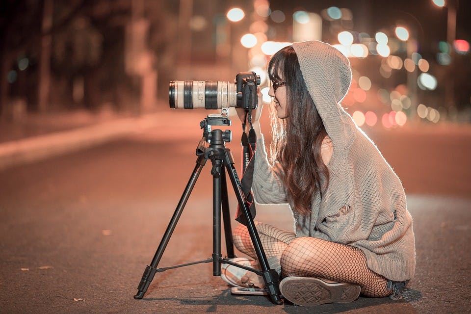 a girl sat on the floor taking a picture with a camera on top of a tripod