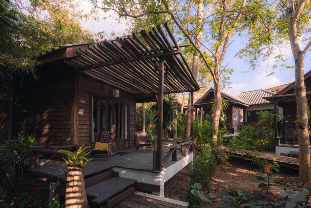 Three wooden houses in a warm country outside being surrounded by trees and plants