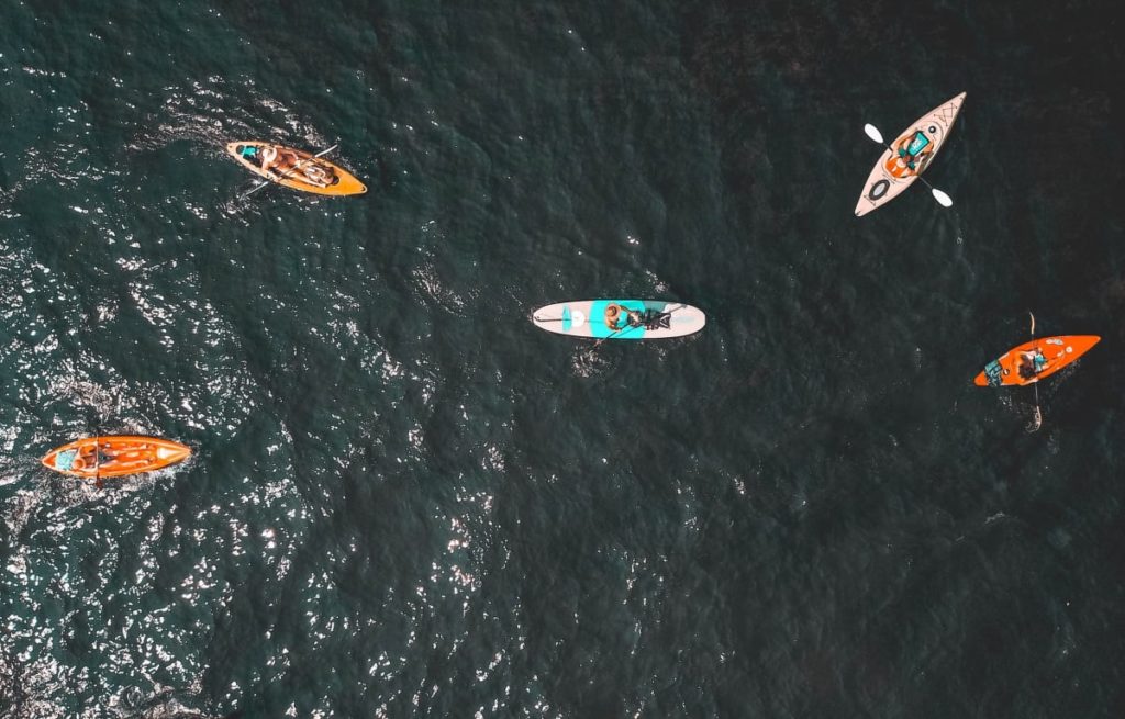 Eine Gruppe Reisepartner fährt mit Kanus auf einem See bei einem Campingplatz