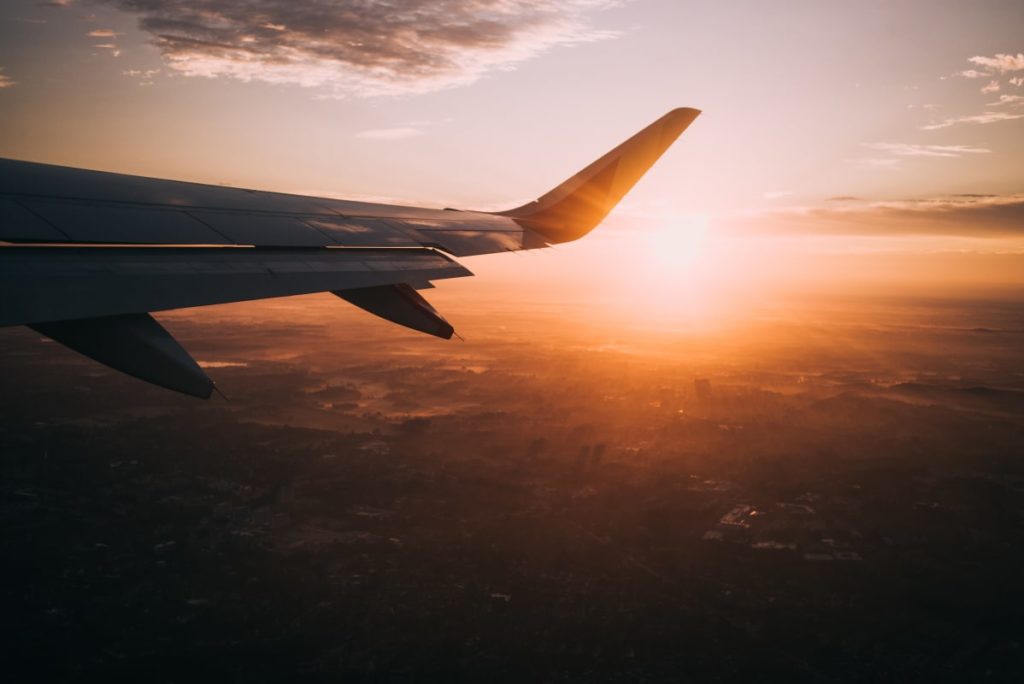 The wing of a plane flying in the sky during the sunset