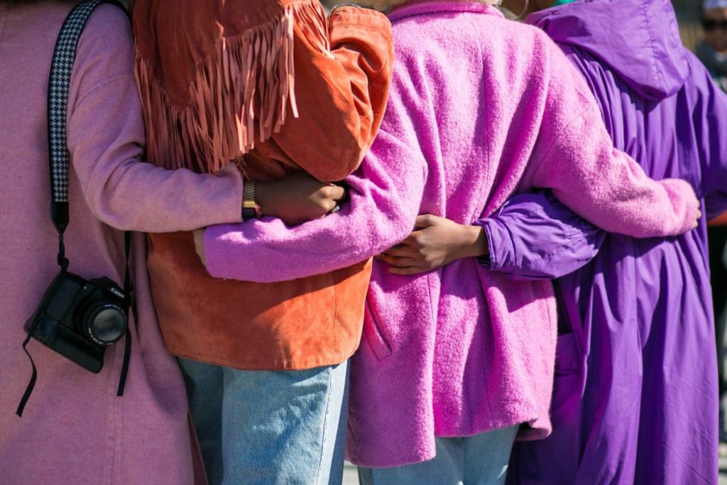 Vier Frauen in pinken und lila Jacken umarmen sich von hinten 