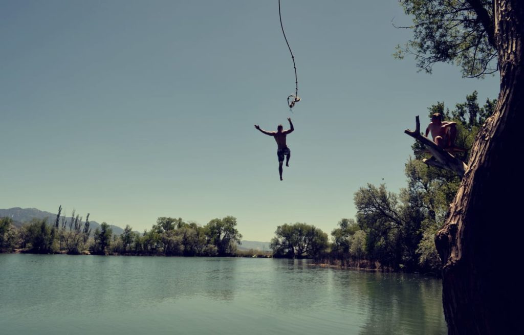 Man jumping into the sea after swinging from a tree