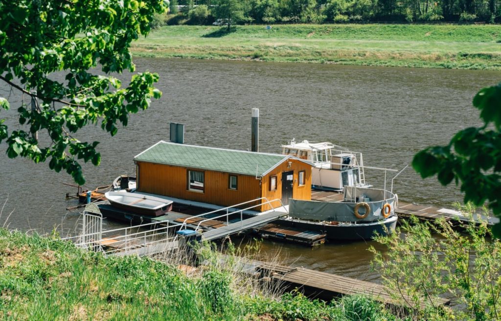 Hölzernes Hausboot mit grünem Dach in der Mecklenburgischen Seenplatte, angelegt an einem kleinen Steg 