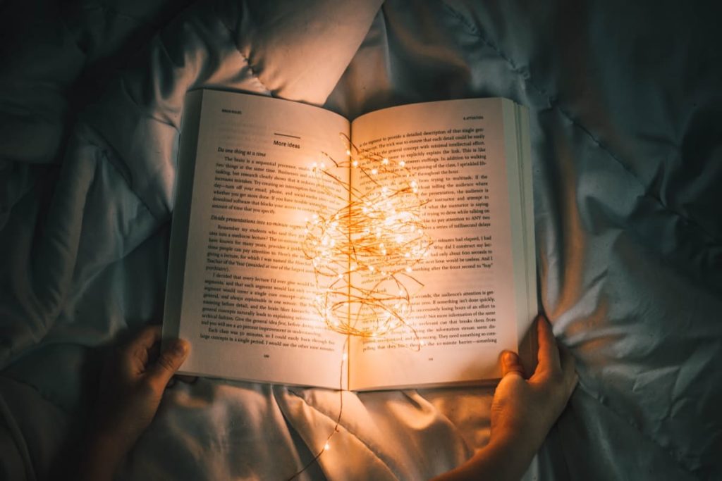 a book being read in bed with fairy lights