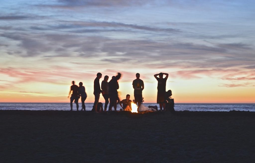 Gruppe von Personen in einer Gruppenreise an einem Lagerfeuer im Sonnenuntergang