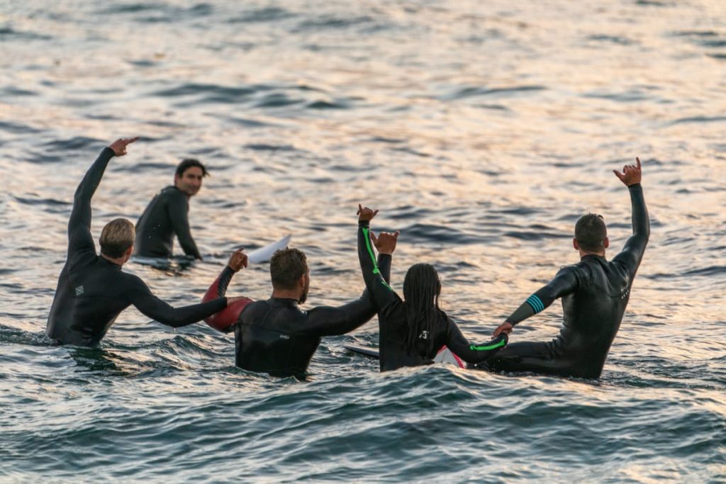 a group of friends surfing in the ocean with all their hands up 